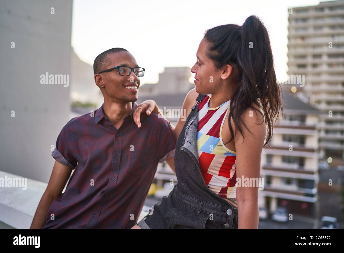Glückliches junges Paar, das auf dem städtischen Dachbalkon spricht Stockfoto