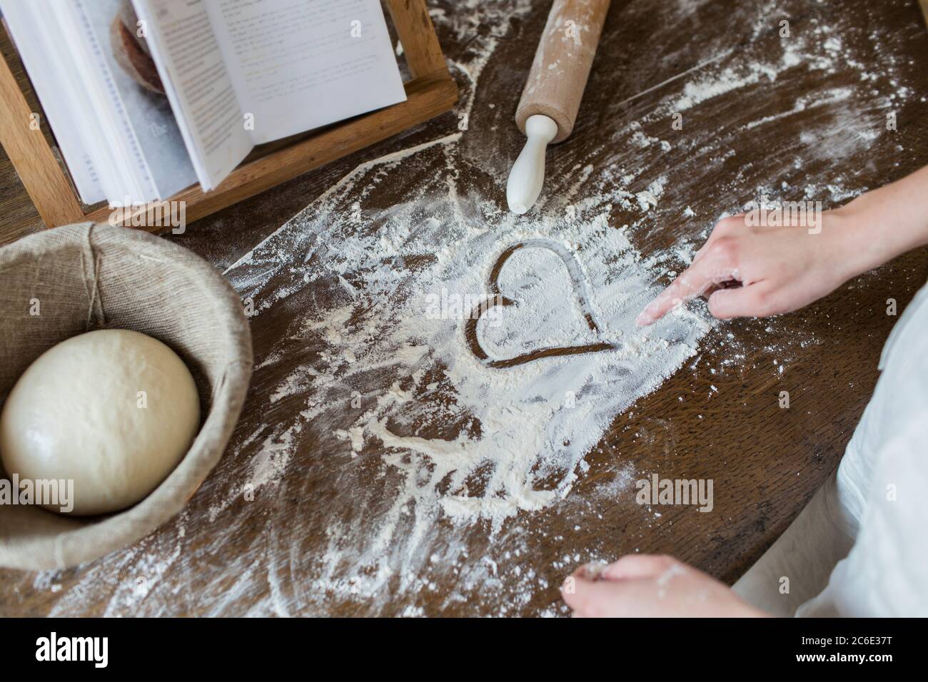 Teenager-Mädchen Zeichnung Herzform in Mehl auf Küchentisch Stockfoto