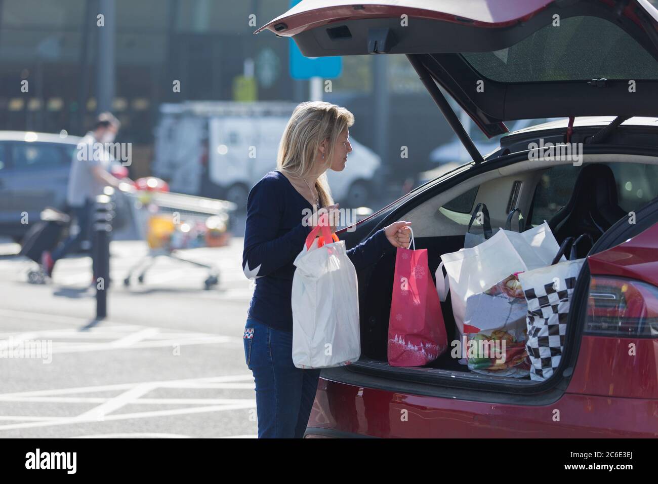Frau lädt Lebensmittel in den hinteren Teil des Autos auf sonnigen Parkplatz Stockfoto