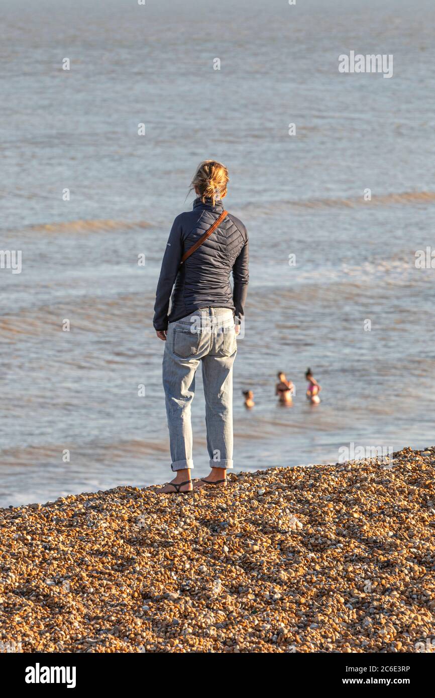 Eine junge Frau, die während der Coronavirus-Pandemie ihre Familie beim Schwimmen im Meer beobachtet Stockfoto