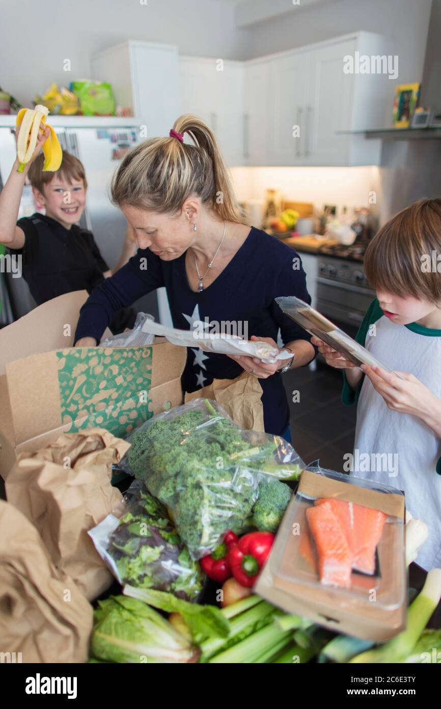 Frau und Söhne entladen frische Produkte aus der Box in der Küche Stockfoto