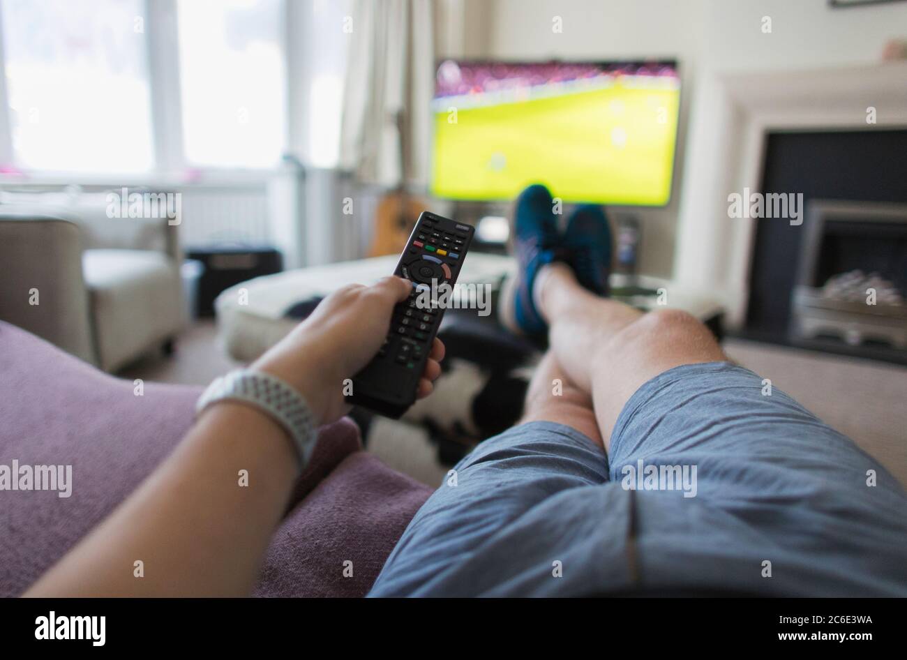 POV Mann mit Fernbedienung beobachten Fußballspiel auf Wohnzimmer Sofa Stockfoto
