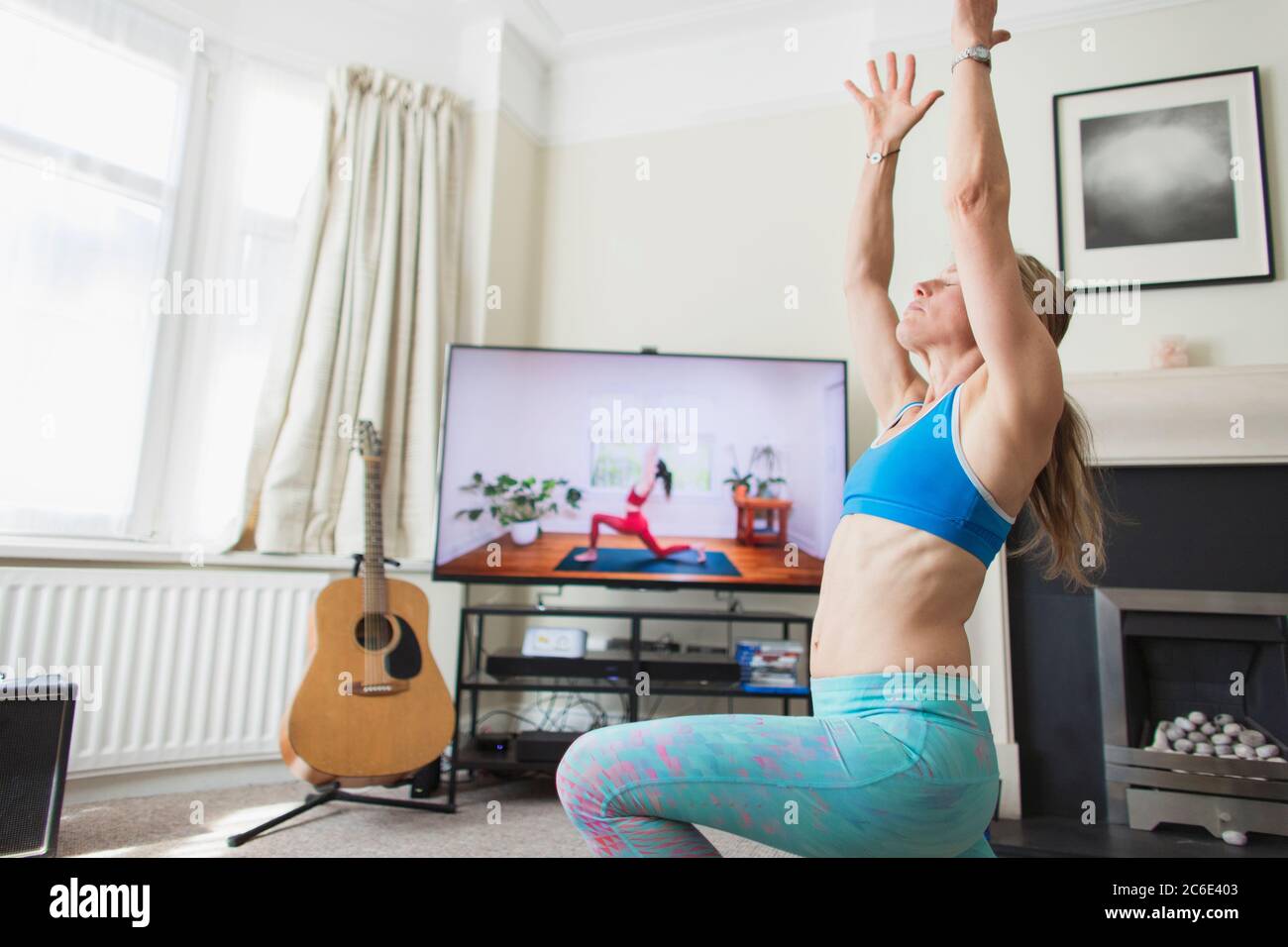 Frau, die Yoga am Fernseher im Wohnzimmer praktiziert Stockfoto