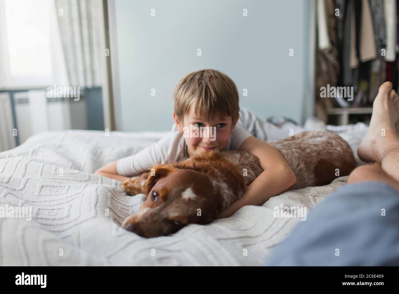 Niedlicher Junge kuschelt mit Hund auf dem Bett Stockfoto