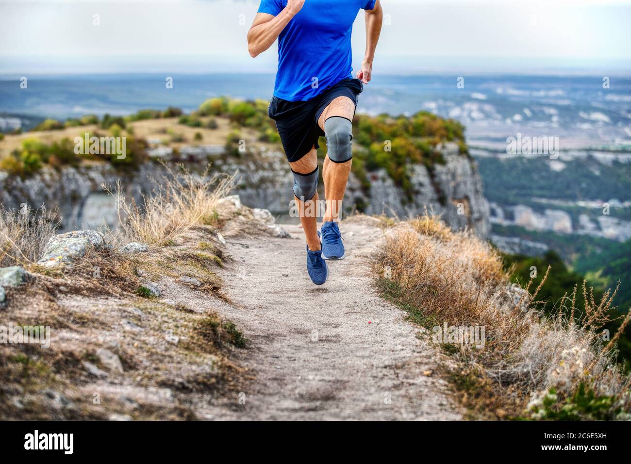Männlicher Läufer in Kniepolstern läuft auf schmalem Bergweg Stockfoto