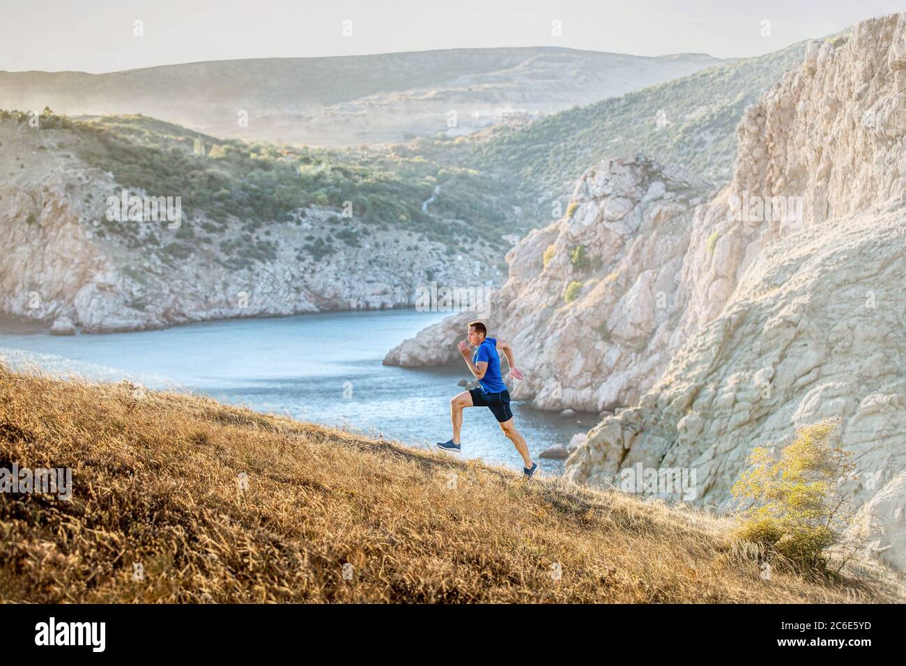 Mann mittleren Alters läuft bergauf auf auf dem Weg im Hintergrund der Meeresbucht und Berge Stockfoto