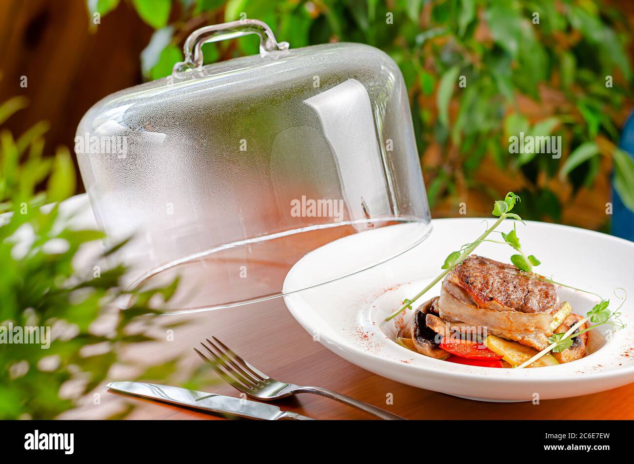 Köstliches Kalbsmedaillon mit Gemüse und Micro Greens auf weißem Teller mit Glaskappe. Konzept der Speisekarte des Restaurants Stockfoto