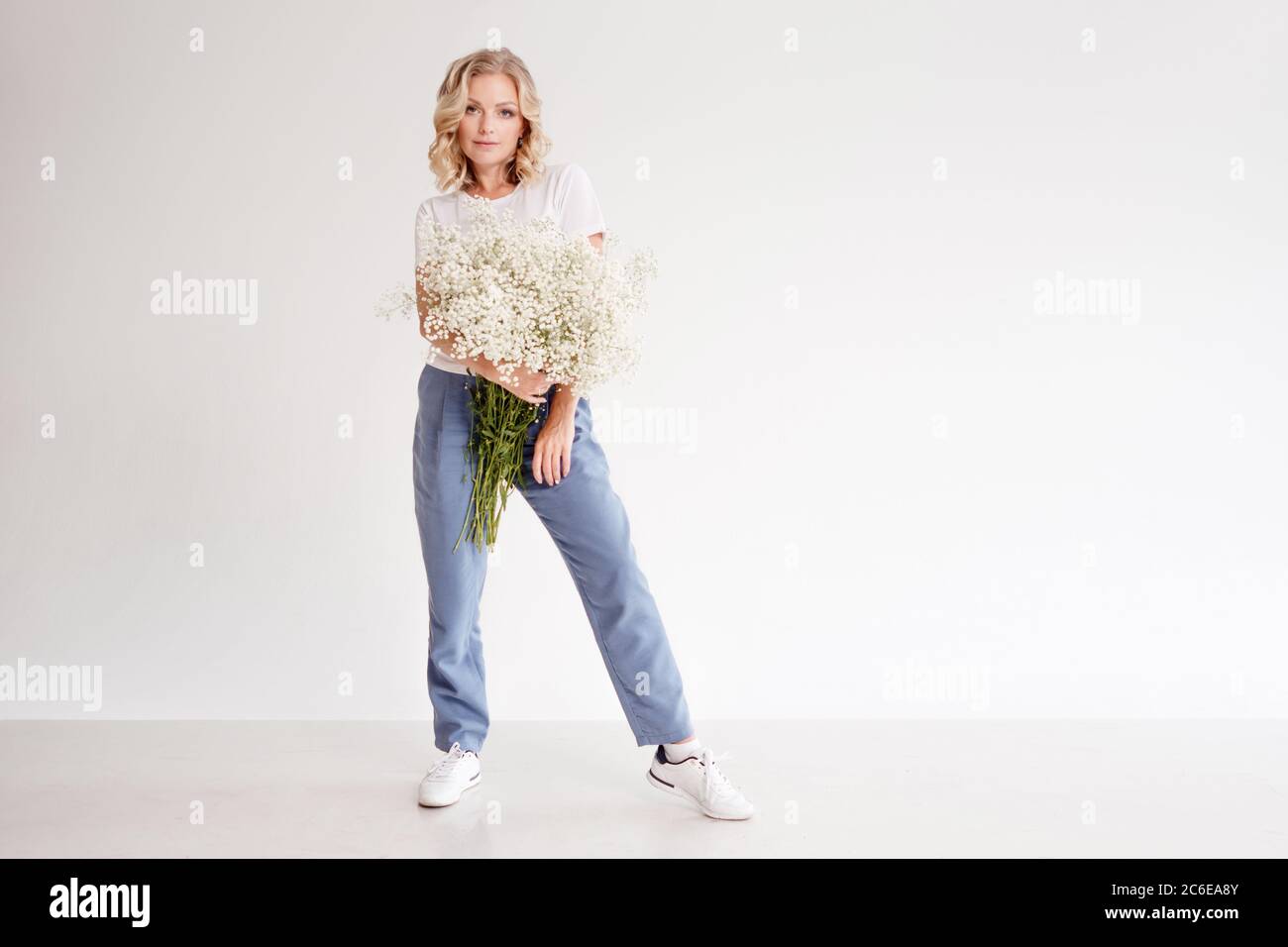 Stilvolle junge blonde Frau mit einem Bouquet von Gypsophila. Porträt auf weißem Hintergrund. Happy Girl mit einem Blumenstrauß, Blumenlieferung. Stockfoto