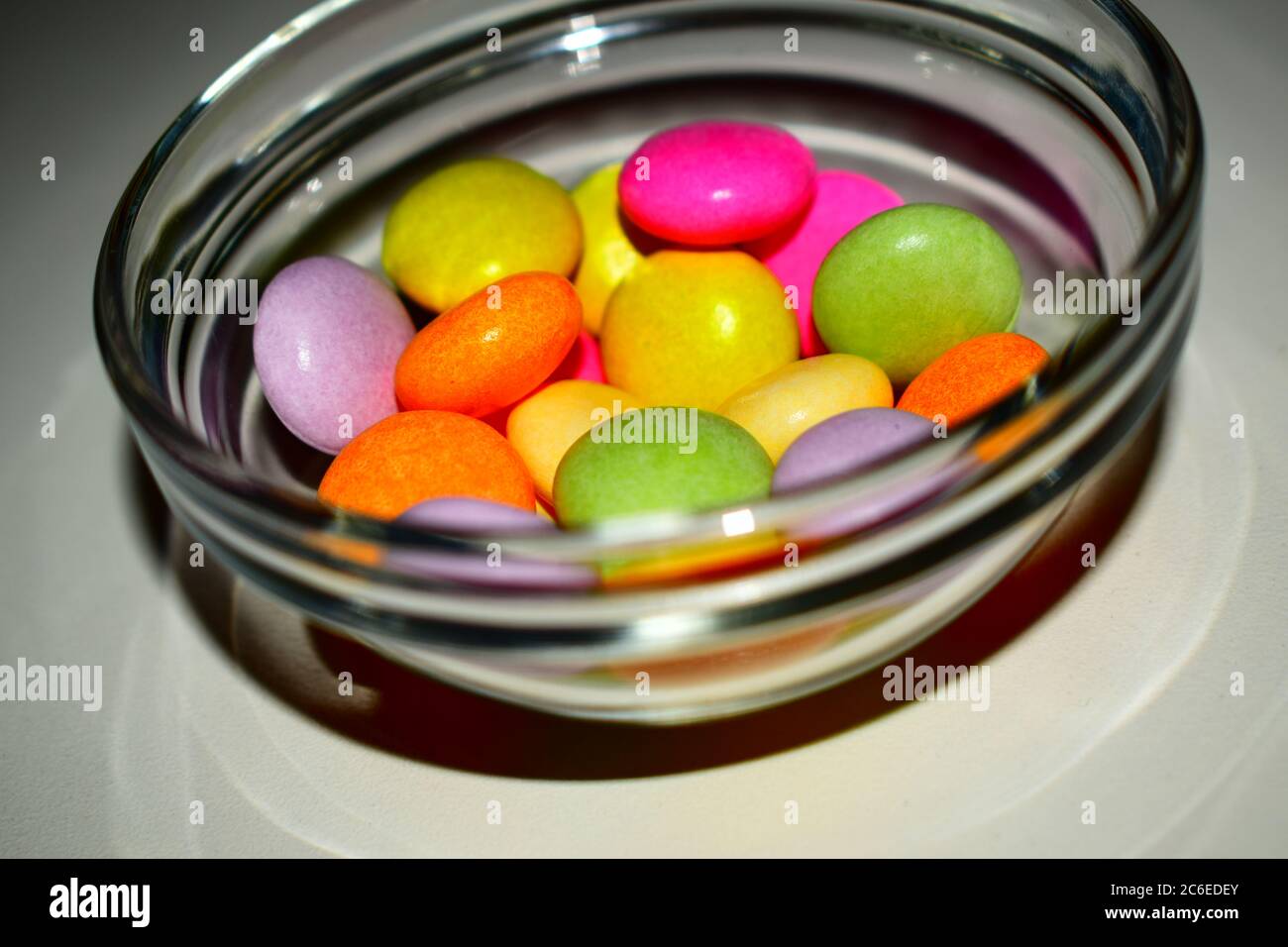 Gruppe von kleinen gemischten farbigen Süßigkeiten in einer transparenten Glasschale auf dem weißen Hintergrund Stockfoto