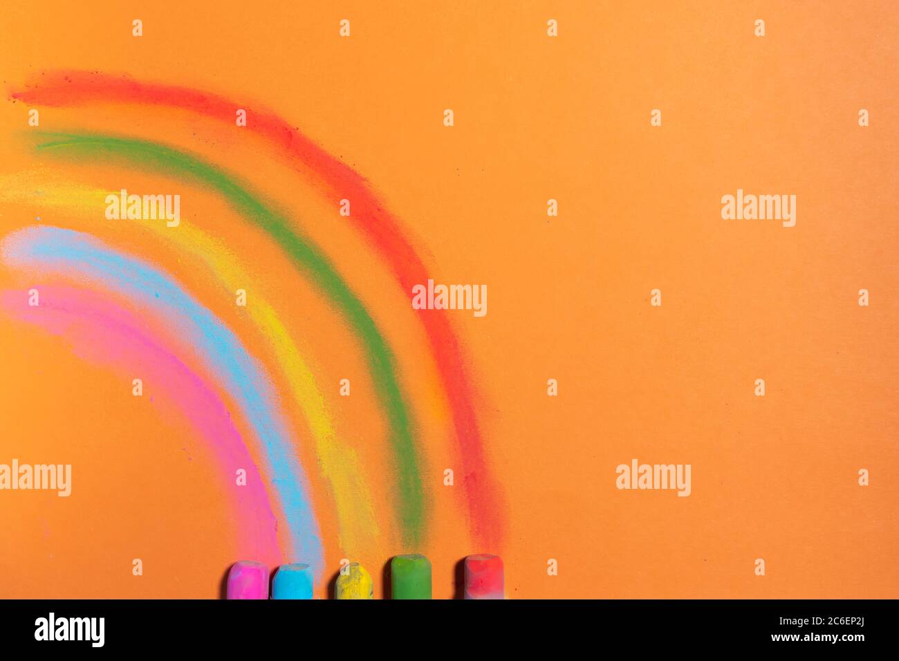 Bunte Kreiden zeichnen einen Regenbogen auf einem orangen Hintergrund Stockfoto