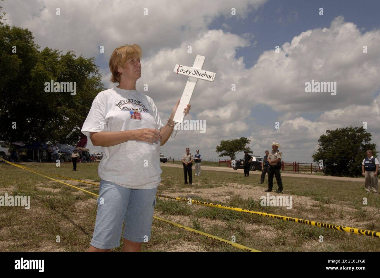 Crawford, Texas, 12. August 2005: Die Antikriegsprotestierende Cindy Sheehan, deren Sohn Casey im Irakkrieg getötet wurde, hält ein weißes Holzkreuz mit dem Namen ihres Sohnes. Sie ist an der Proteststätte „Camp Casey“, wo etwa 100 Demonstranten gegen den Krieg im Irak während des Augusturlaubs von US-Präsident George W. Bush auf seiner nahegelegenen Ranch eine Mahnwache halten. Sie beobachtet, wie die Kutsche des Präsidenten vorbeifährt, als er zu einer Spendenaktion ging. ©Bob Daemmrich Stockfoto