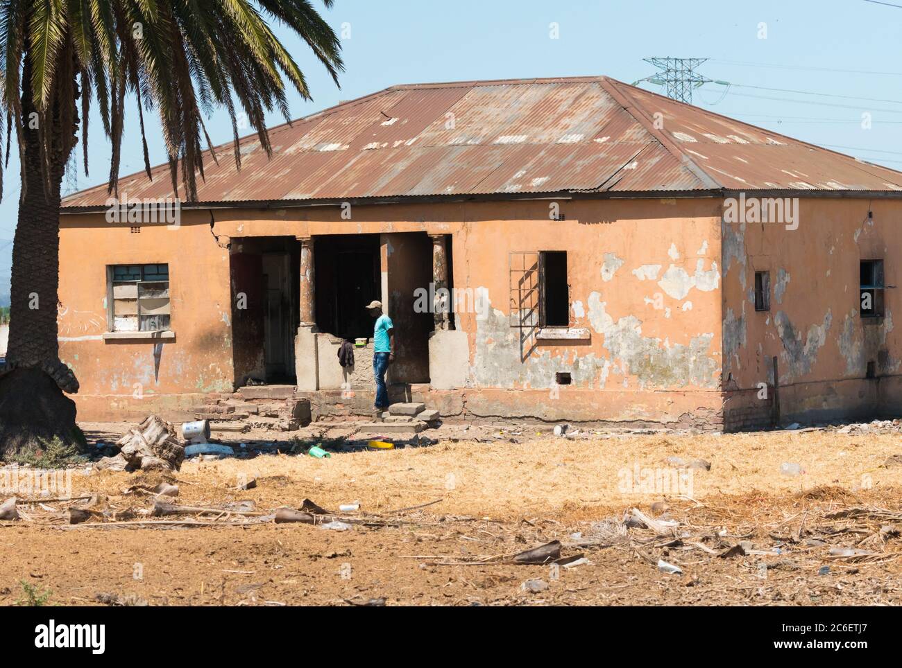 Altes, heruntergefalles, vernachlässigtes Haus mit einem Afrikaner, der draußen steht und Armut und schlechte Lebensbedingungen in der Stadt Kapstadt, Südafrika, zeigt Stockfoto