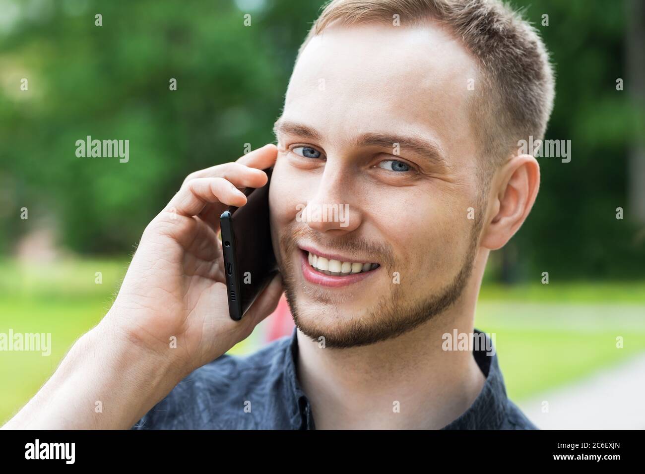 Porträt eines hübschen jungen Mannes, der im Park spazierengeht und auf dem Handy spricht. Mann, der auf dem Handy spricht, Nahaufnahme. Stockfoto