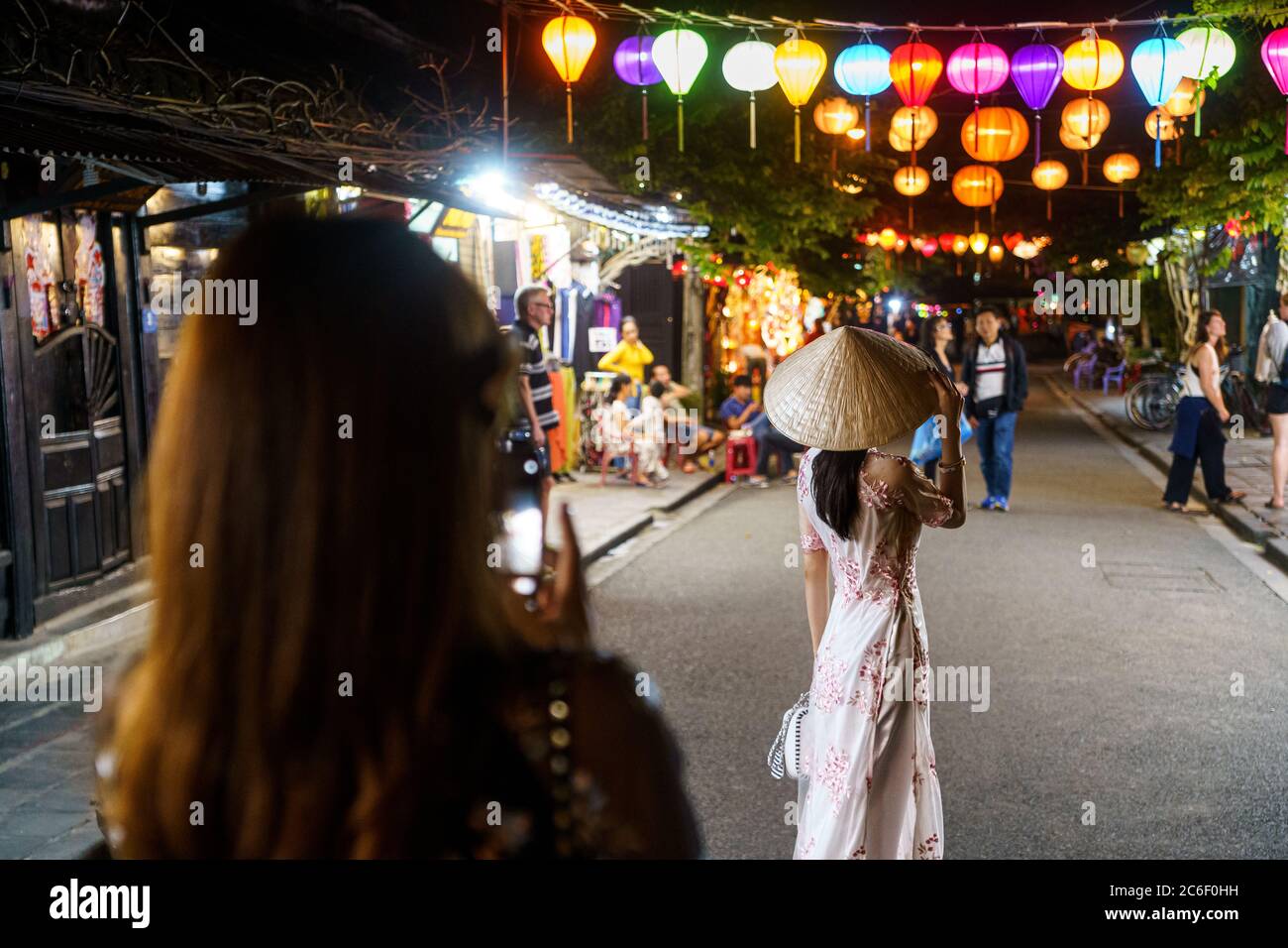 Asiatische Frau, die während der hoi an Nacht eine Frau in weißem vietnamesischem Kleid auf der Straße fotografiert Stockfoto