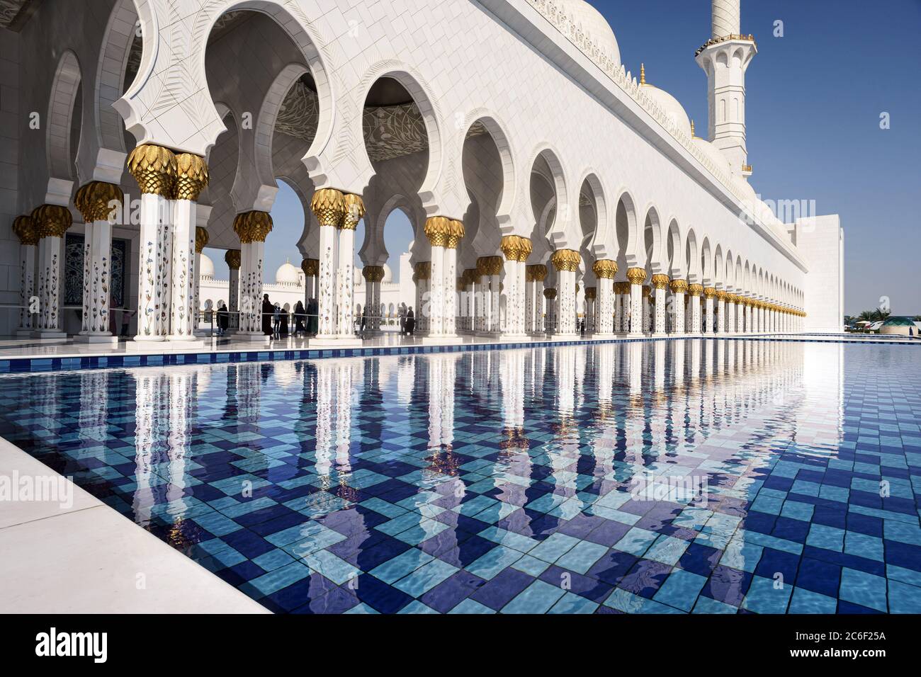 Blick auf die weißen Säulen der Abu Dhabi Moschee, die sich an einem sonnigen Tag mit blauem Himmel im Wasser des Pools spiegeln Stockfoto