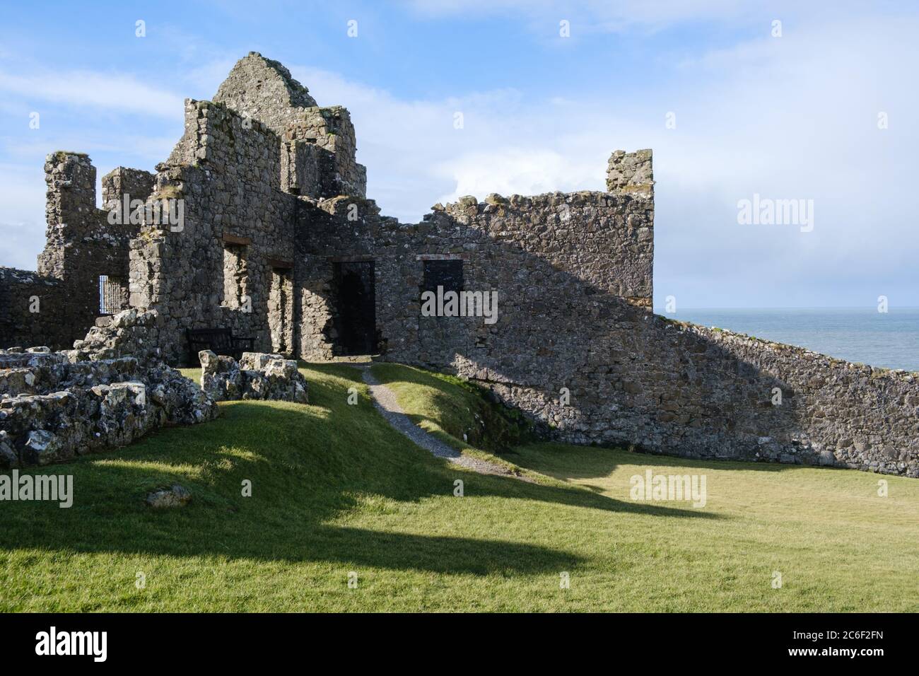 Dunluce Castle ruiniert vor einem wunderschönen hellblauen Himmel, inmitten üppig grünen Grases, in der Nähe von Portrush in Co. Antrim, Nordirland. Stockfoto