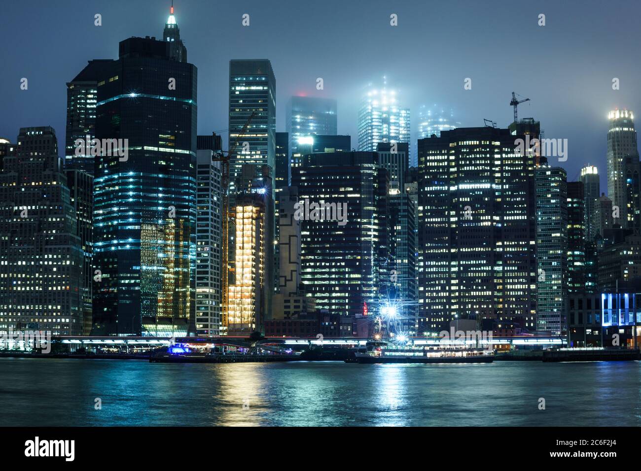 Blick auf die Insel Manhattan bei Nacht mit Licht von Gebäuden, die sich an einem nebligen Tag vom Wasser abspiegeln Stockfoto
