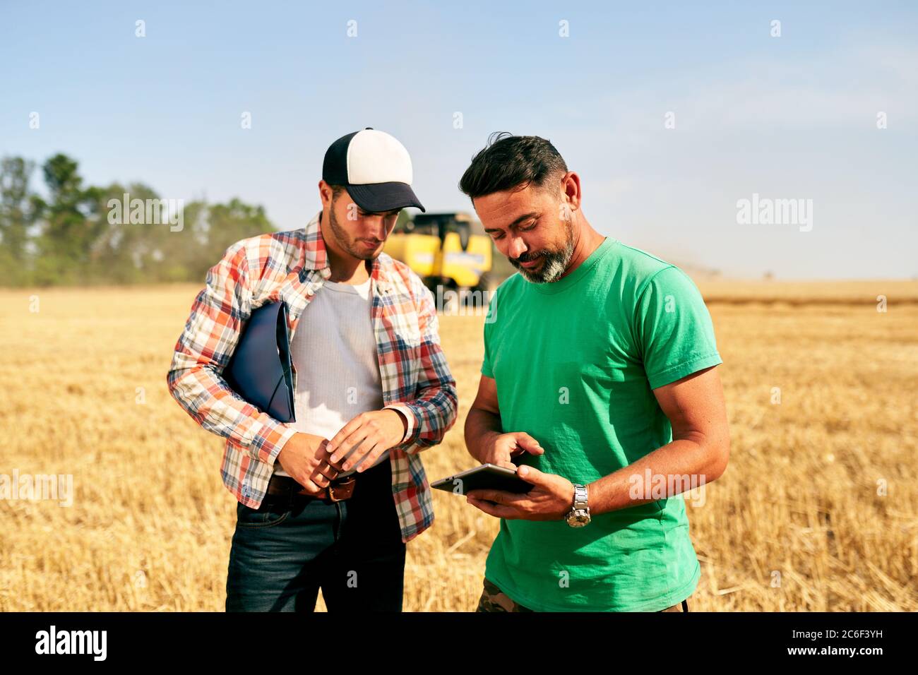 Zwei Bauern stehen im Weizenstoppelfeld, diskutieren Ernte, Ernte. Senior Agronom mit Touch Tablet pc lehrt junge Mitarbeiter. Innovative Technik Stockfoto