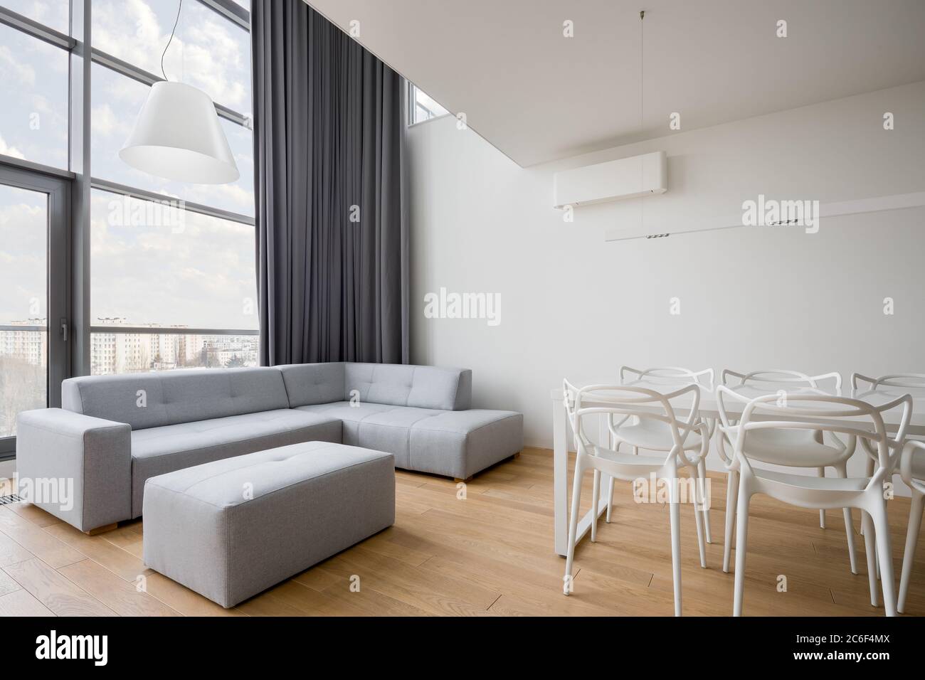Modernes Wohnzimmer mit weißem Tisch, grauem Sofa und Fensterwand Stockfoto