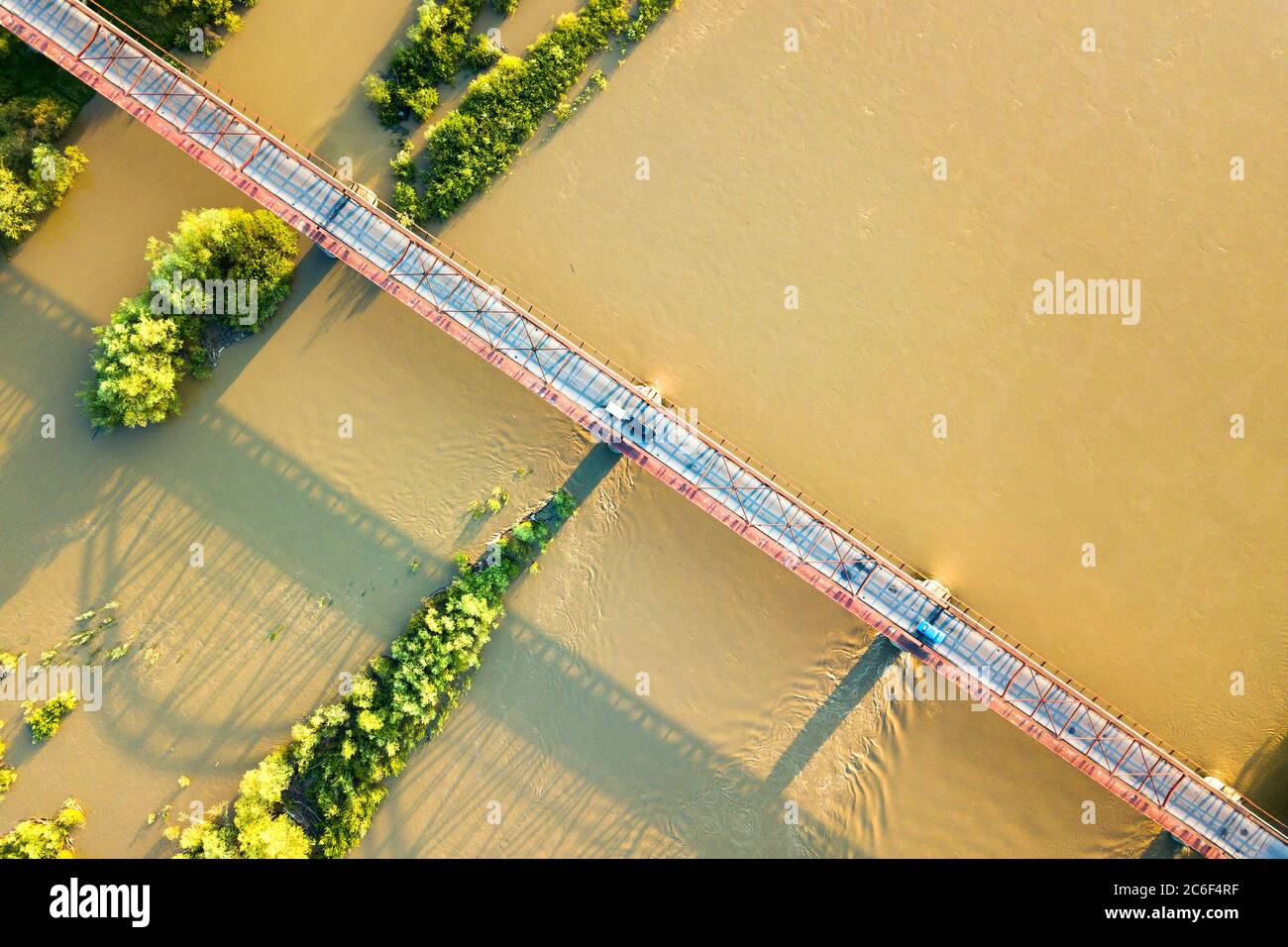 Luftaufnahme einer schmalen Straßenbrücke, die sich über einen schlammigen, breiten Fluss in grüner ländlicher Umgebung erstreckt. Stockfoto