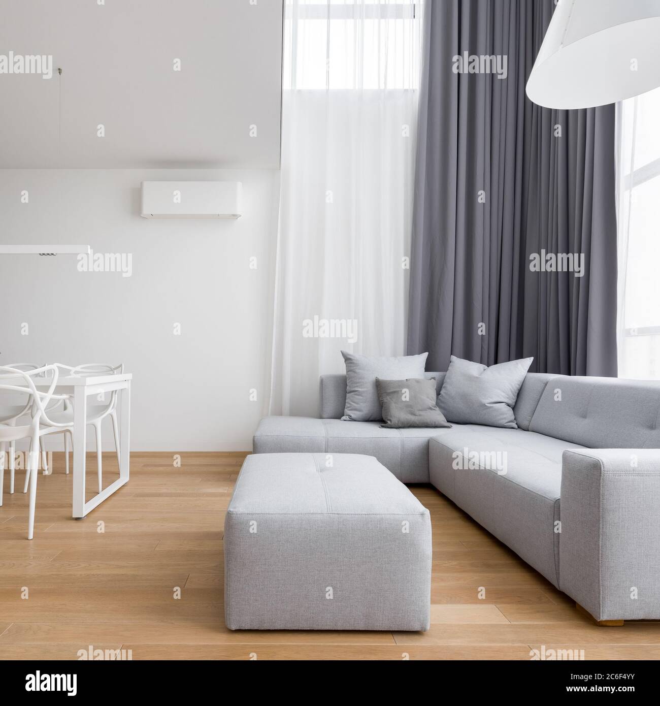 Wohnzimmer im minimalistischen Design mit grauem Ecksofa und langen Fenstervorhängen Stockfoto