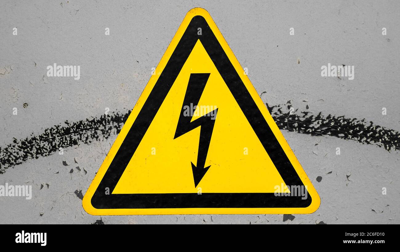 Schmutziges gelbes Hochspannungswarnschild auf grauem Hintergrund isoliert Stockfoto