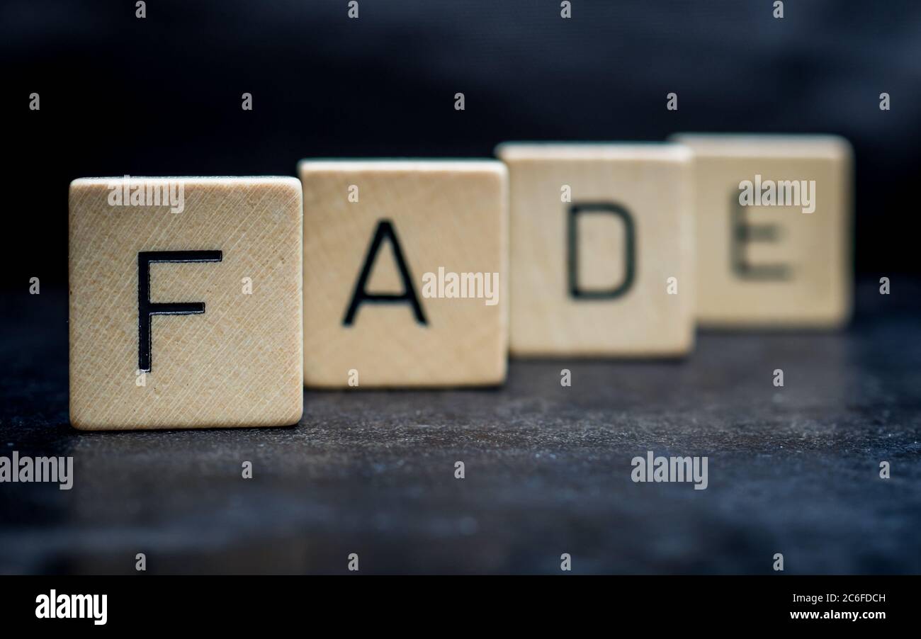 Stehende hölzerne Buchstabenfliesen bilden Wörter auf einer grauen Gusseisenoberfläche im Hintergrund, verblassen, nah oben Stockfoto