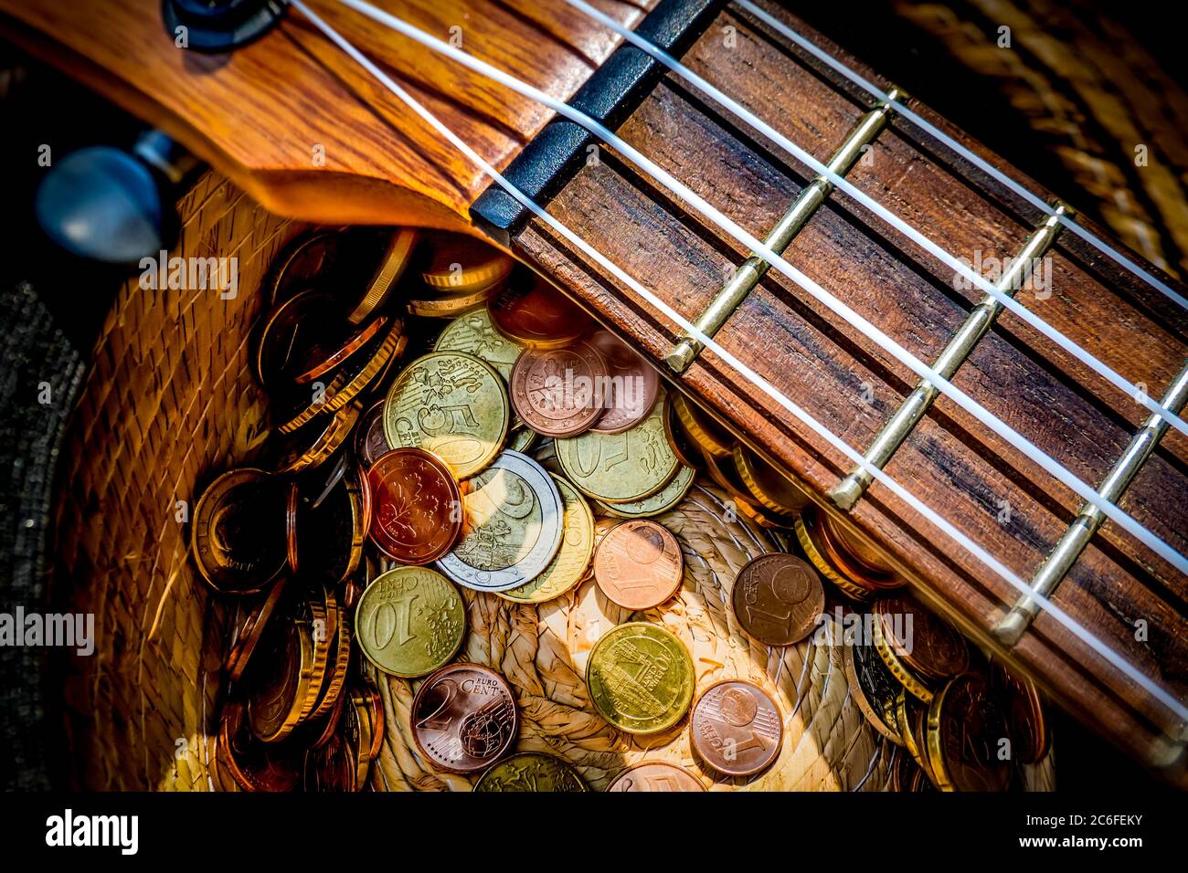 hut mit gespendeten Münzen und Ukulele-Musikinstrument auf der Oberseite, Geld verdienen mit Straßenmusik im Sonnenlicht Stockfoto