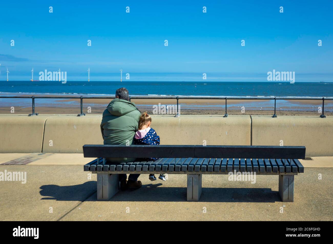 Genießen Sie die Sonne ein Mann und ein kleines Mädchen sitzen in seiner Nähe auf einer Bank mit Blick auf das Meer auf Redcar Esplanade Stockfoto