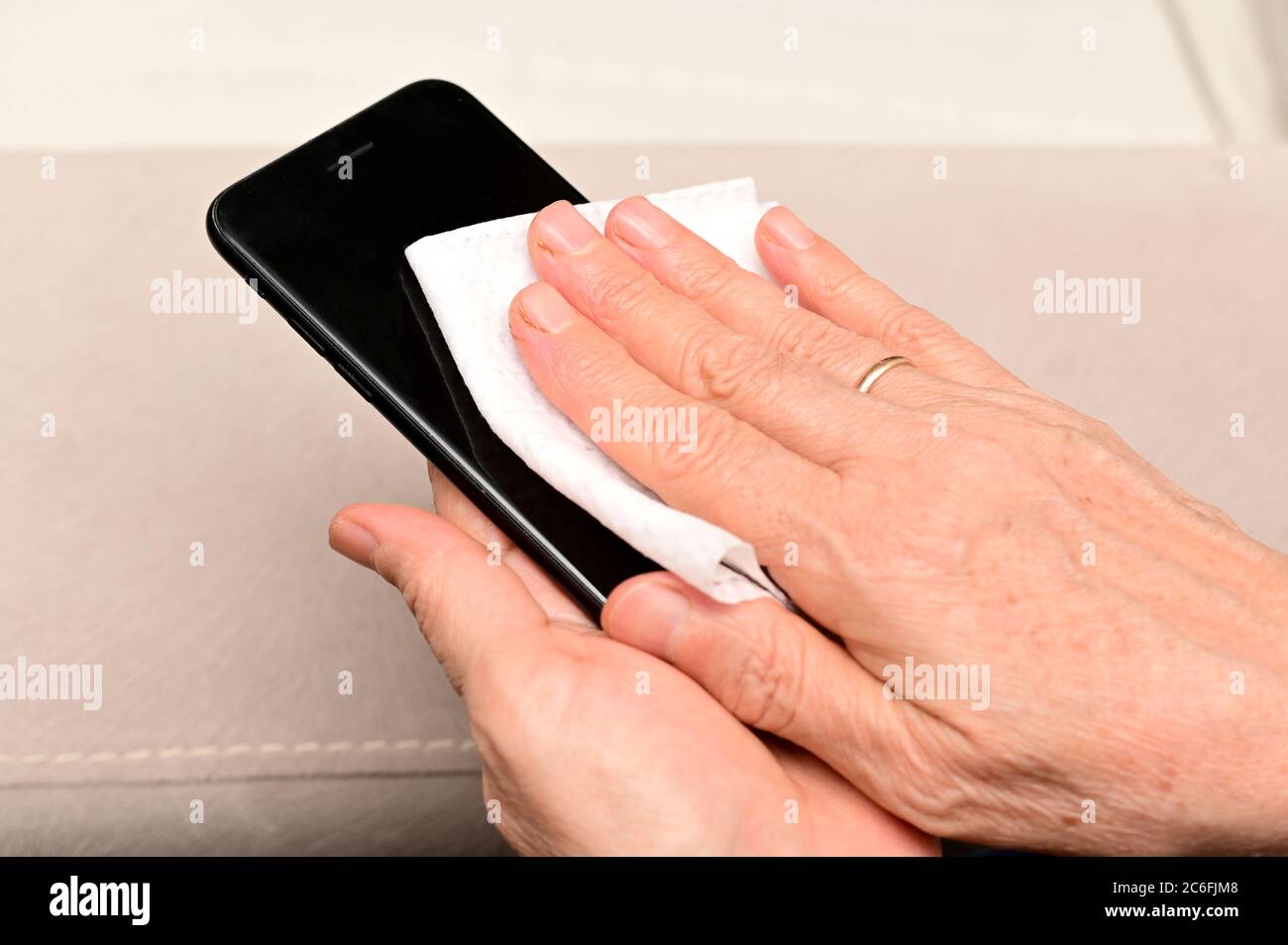 Ältere Frau putzt ihren Smartphone-Bildschirm, um Keime zu beseitigen, covid-19 mit Alkohol. Stockfoto