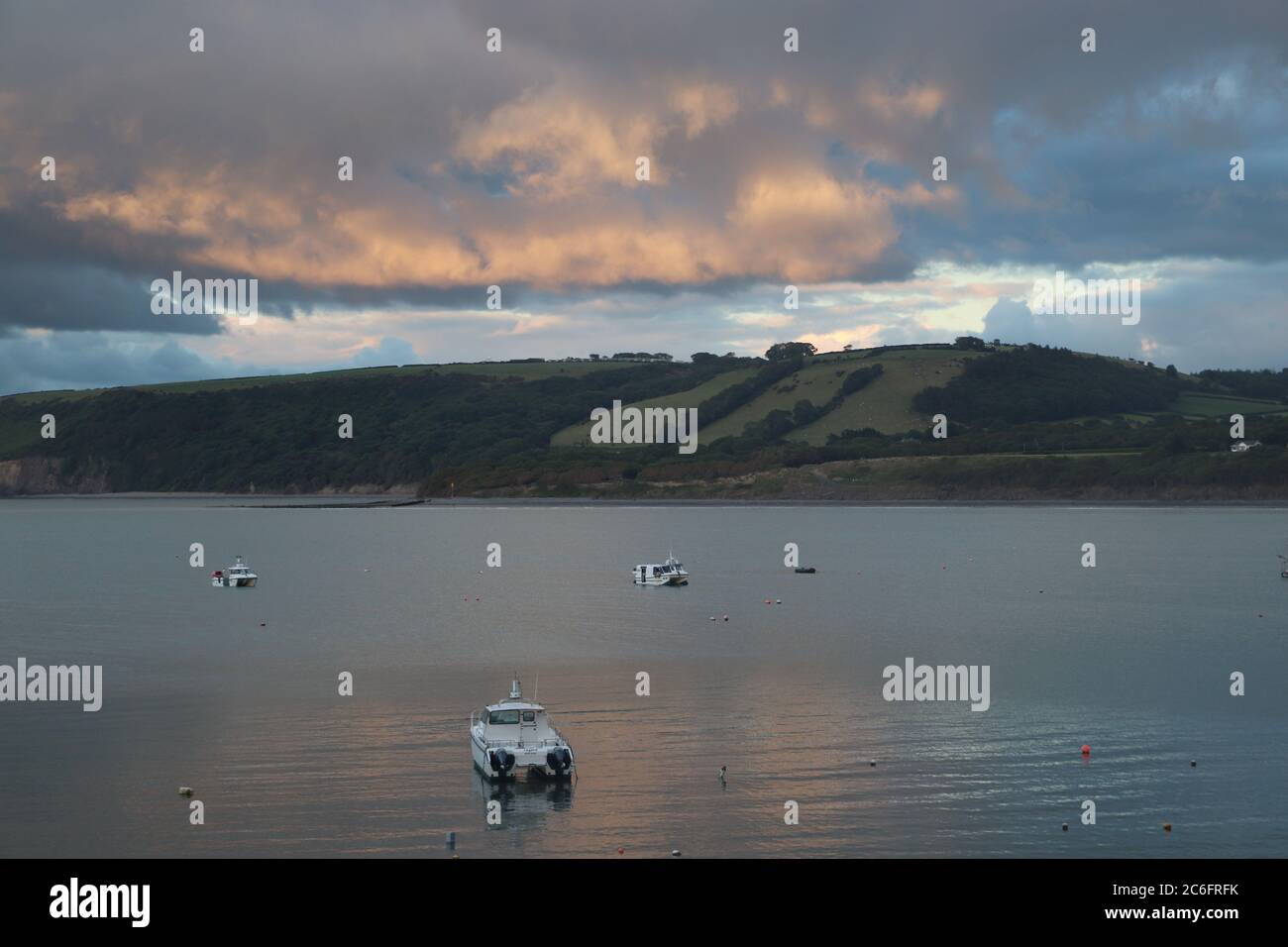 Ruhige Bucht mit Booten und grünen Hügeln im Hintergrund bei Dämmerung Stockfoto