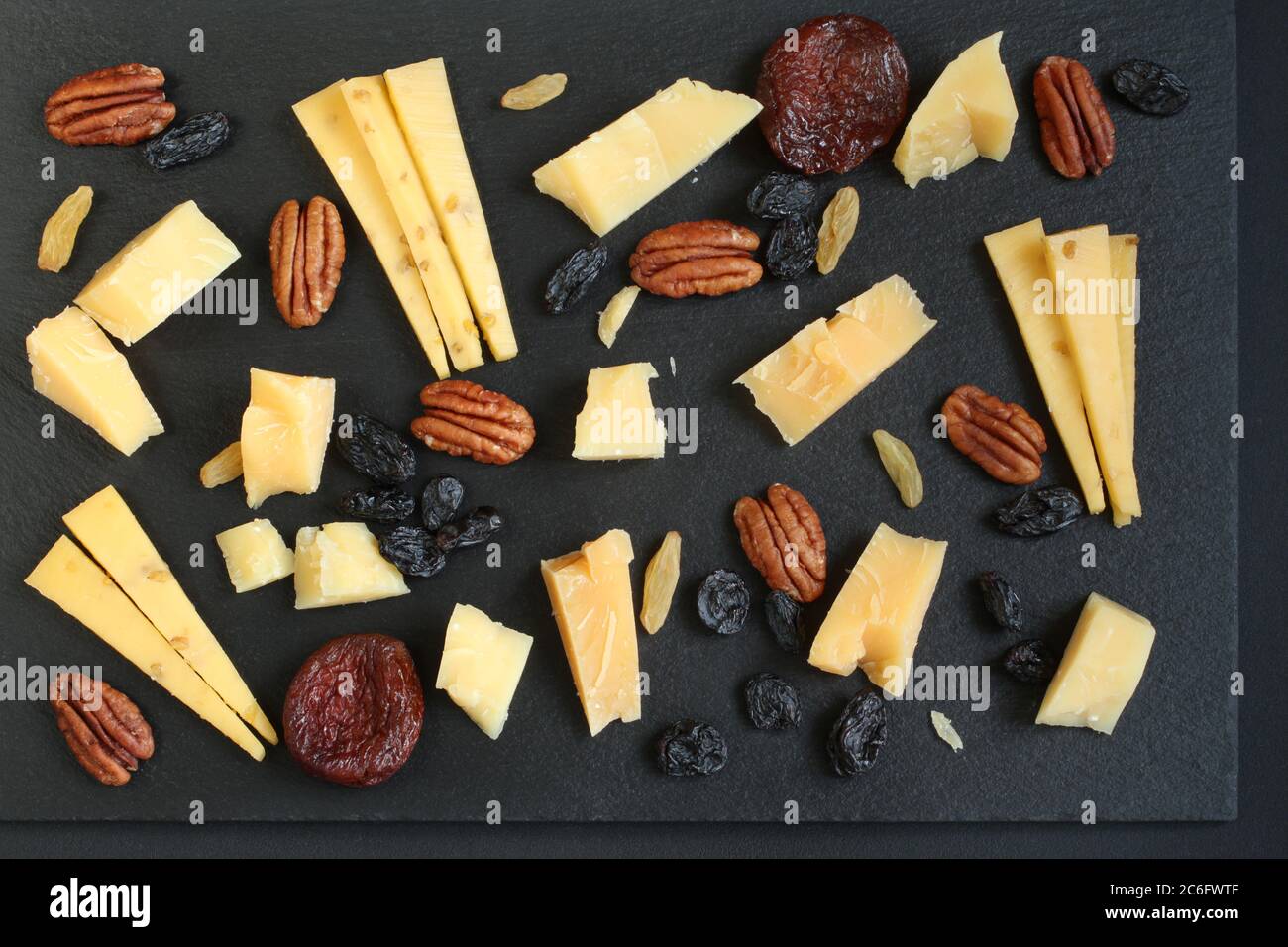 Parmesankäse und gouda mit Bockshornklee, blauen und goldenen Rosinen und getrockneten Aprikosen auf schwarzem Steinteller auf schwarzem Tisch. Nahaufnahme. Oben- Stockfoto