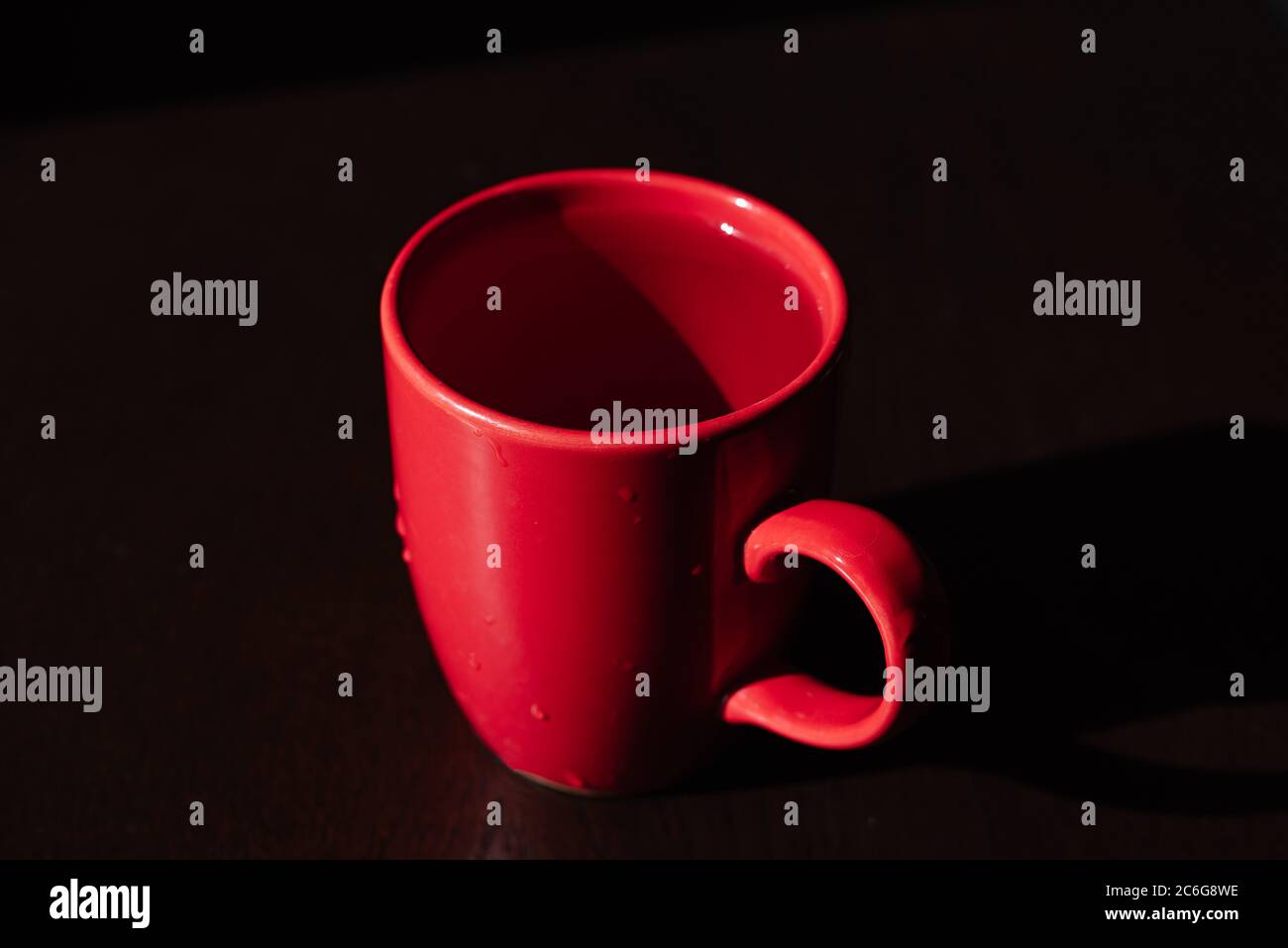 Roter Becher auf dem Tisch, durchsichtige Flüssigkeit in der Tasse, ein Objekt im Schatten Stockfoto