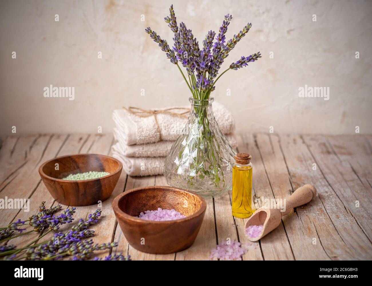 Flasche mit ätherischem Öl, Handtücher und Schalen mit Meersalz auf Holztisch. Lavendel Kosmetik, Spa und Wellness-Konzept. Stockfoto