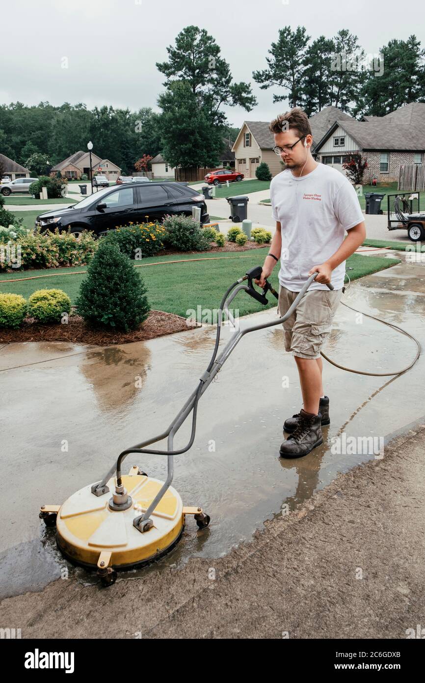 Man Druckwäsche oder Powerwashing oder Reinigung einer Betoneinfahrt und Bürgersteig in Montgomery Alabama, USA. Stockfoto