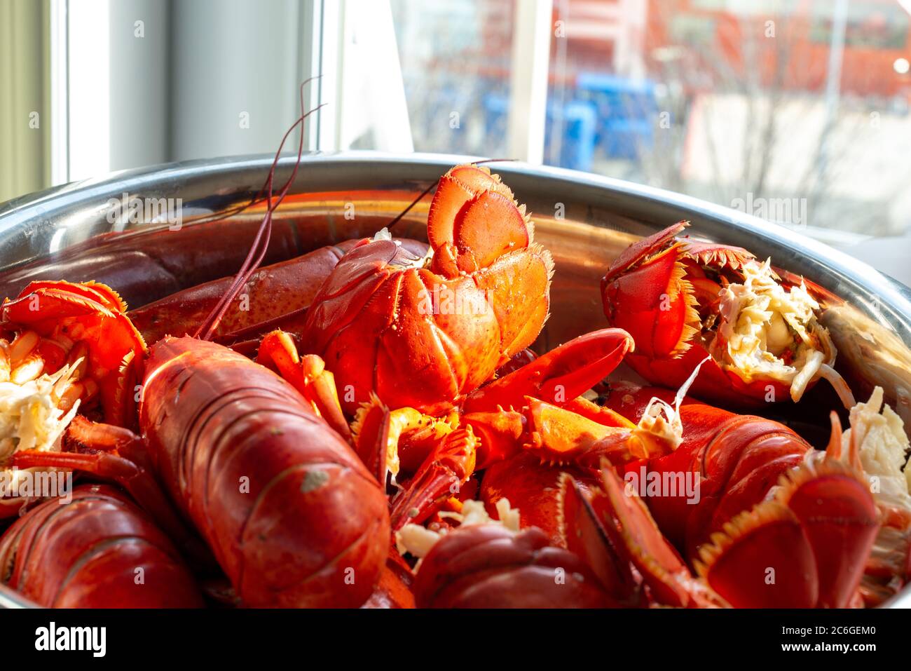 Eine große Aluminiumschale mit gekochtem Hummer auf einem Tisch in einem Restaurant. Die roten Muscheln haben lange Körper, fünf Paar Beine, zwei Klauen und einen langen Schwanz. Stockfoto