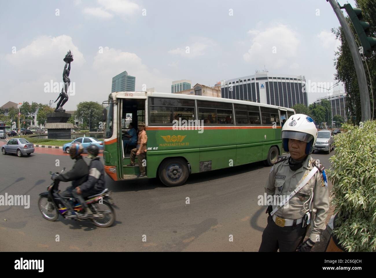 Bus vorbei Polizist am Kreisverkehr mit Patung Pemuda Youth Monument Statue auch bekannt als Pizza man Statue, Jakarta, Indonesien Stockfoto