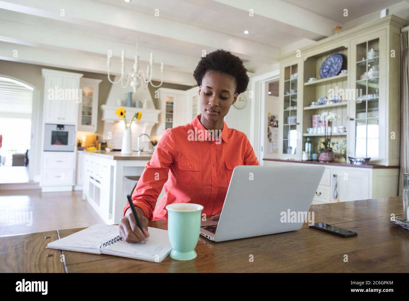 Frau, die sich Notizen gemacht hat, während sie in der Küche einen Laptop benutzt Stockfoto