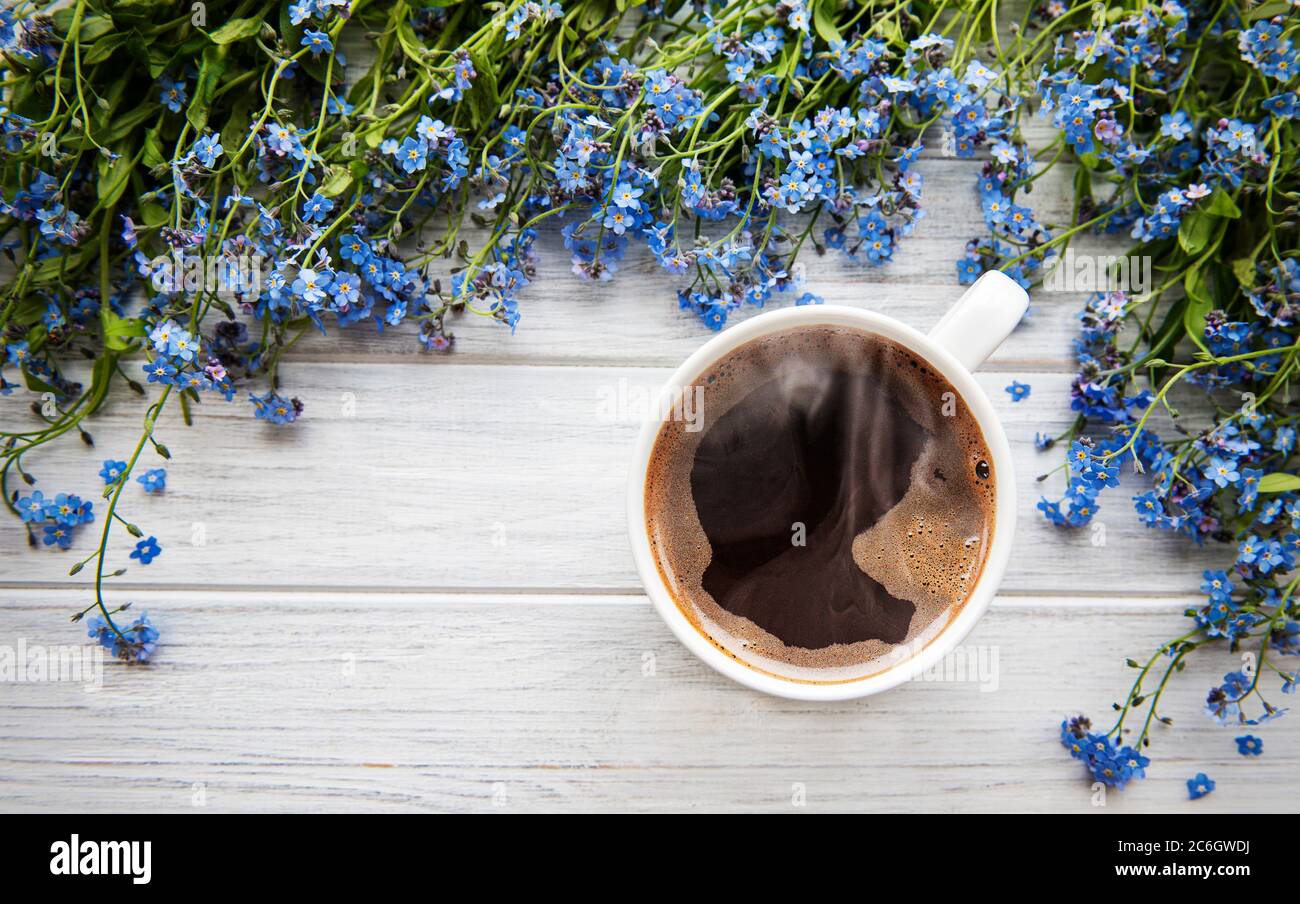 Blaue Vergiss-mich-nicht Blumen und eine Tasse heißen Kaffee auf einem weißen Holztisch Stockfoto