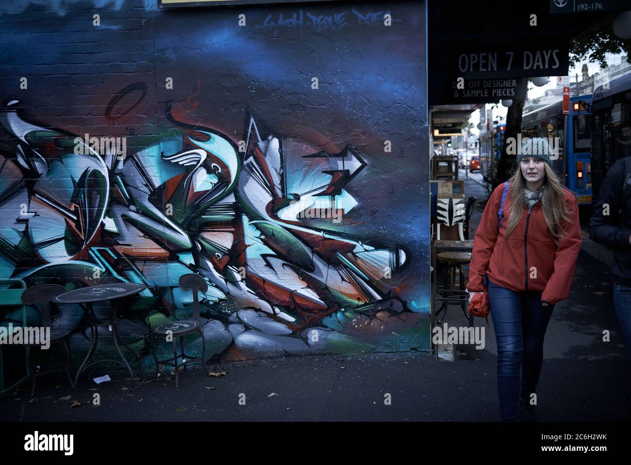 Straßenfotografie. Eine Frau mit rotem Mantel, die an einem Wandbild mit Street Art-Graffiti in Sydney, Australien, vorbeiläuft. Stockfoto