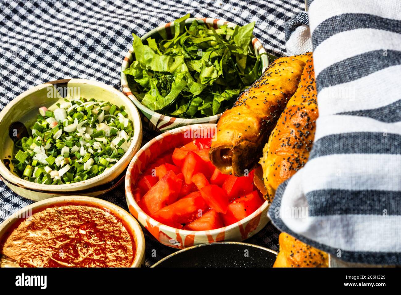 Rustikale Zusammensetzung mit Würstchenbrötchen und verschiedenen Schüsseln mit Sauce und gehacktem Gemüse (Tomaten, grüner Salat, grüne Zwiebel, grüner Knoblauch) Stockfoto