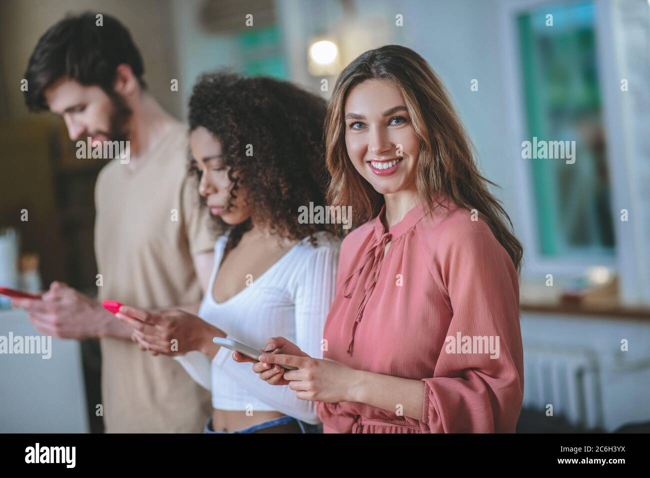 Lächelndes Mädchen in rosa Kleid, Freundin mit Freund Blick auf Smartphones Stockfoto