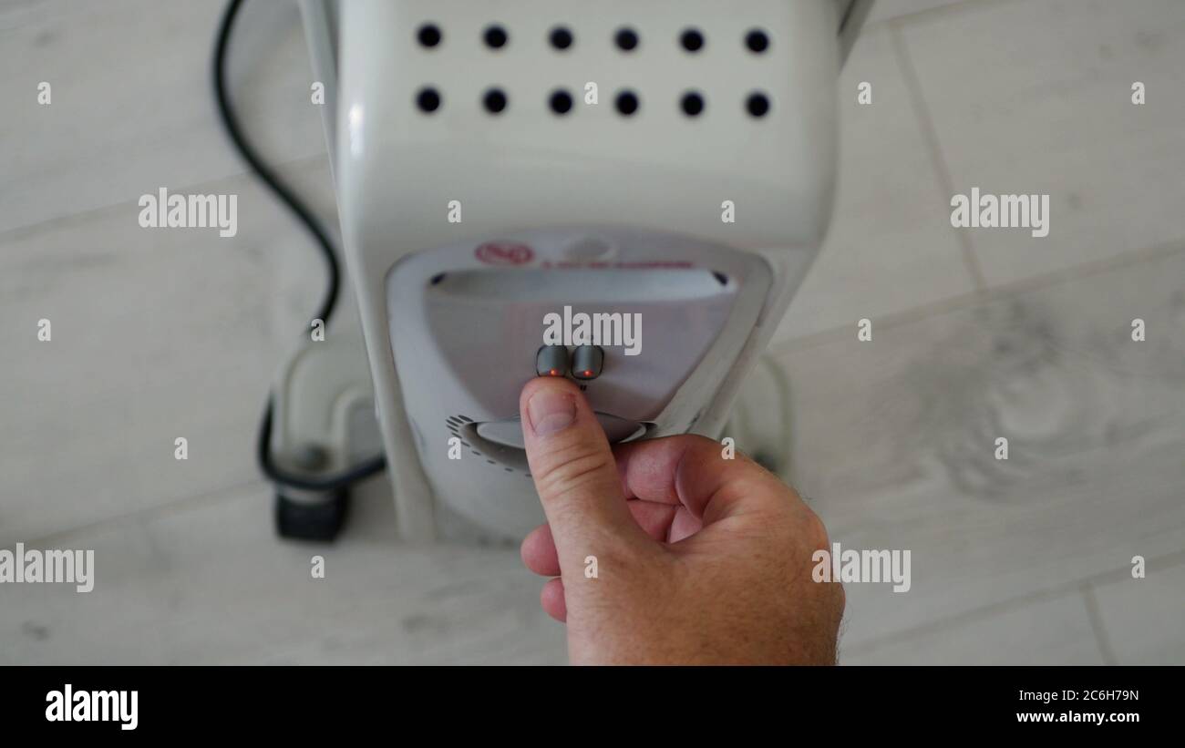 Man stellt die Heiztemperatur eines elektrischen Heizkörpers zu Hause in einem kalten Raum ein Stockfoto