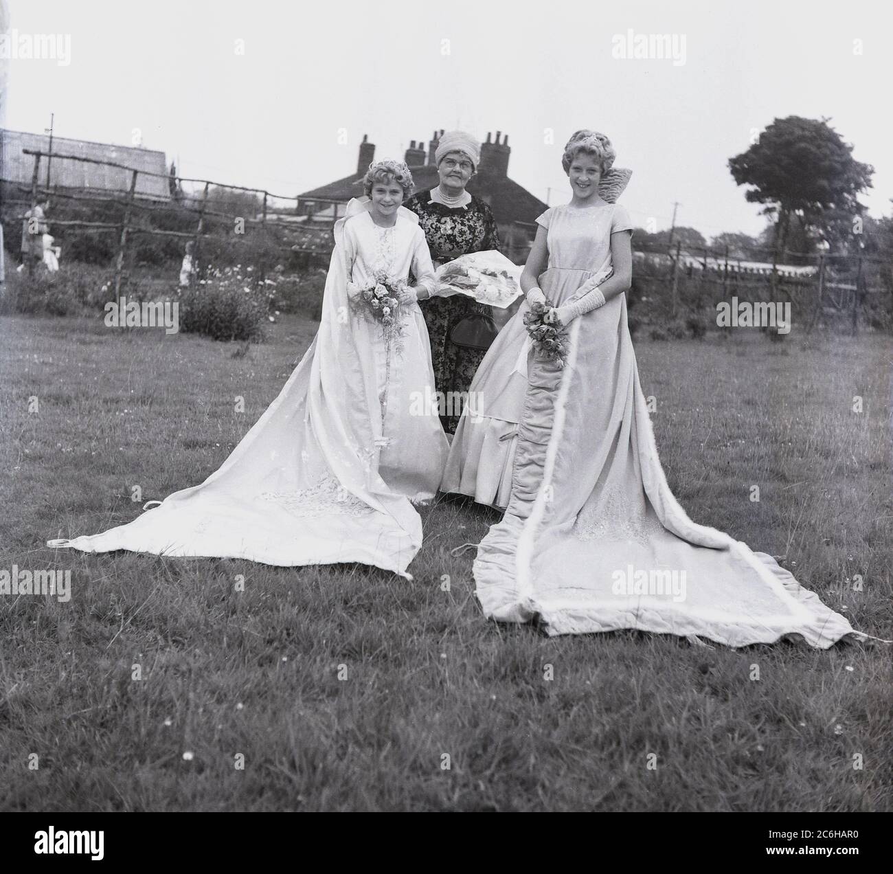 1950er Jahre, historische, lokale Teenager-Mädchen, die Rose Queen und ihr Präzedenzfall, stehen in einem Parkfeld in ihren Gewändern in Farnworth, Bolton, Lancashire, England, Großbritannien. Das jährliche Rose Queen Festival, das im Juni in den 1880er Jahren stattfand, wurde nach den Kriegen der Rosen von 1455-87 zu einem wichtigen jährlichen Ereignis in vielen Städten und Dörfern in ganz Großbritannien, insbesondere in Lancashire, dem sogenannten Red Rose County. Stockfoto