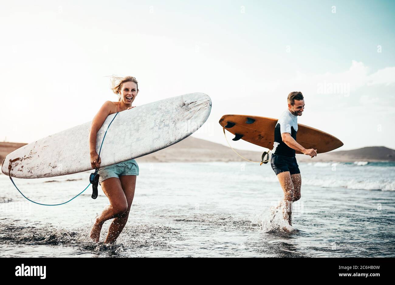 Surfer Paar, dass zusammen mit surfbrettern am Strand bei Sonnenuntergang - Sportliche Freunde Spaß zu surfen. Stockfoto