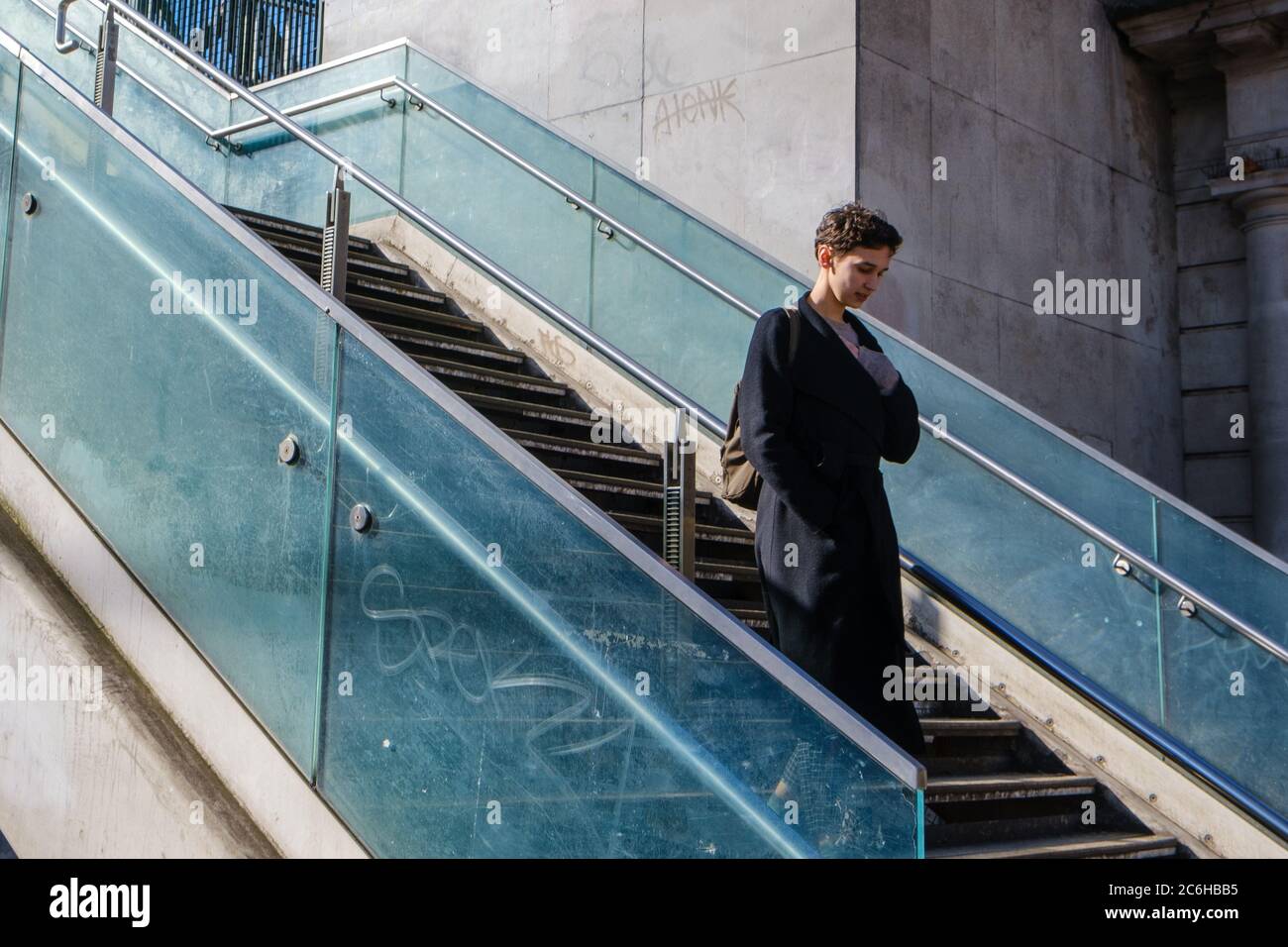 Elegant gekleidete junge Dame in schwarzem Mantel geht die blaue gläserne Treppe im Temple Tube in London hinunter Stockfoto