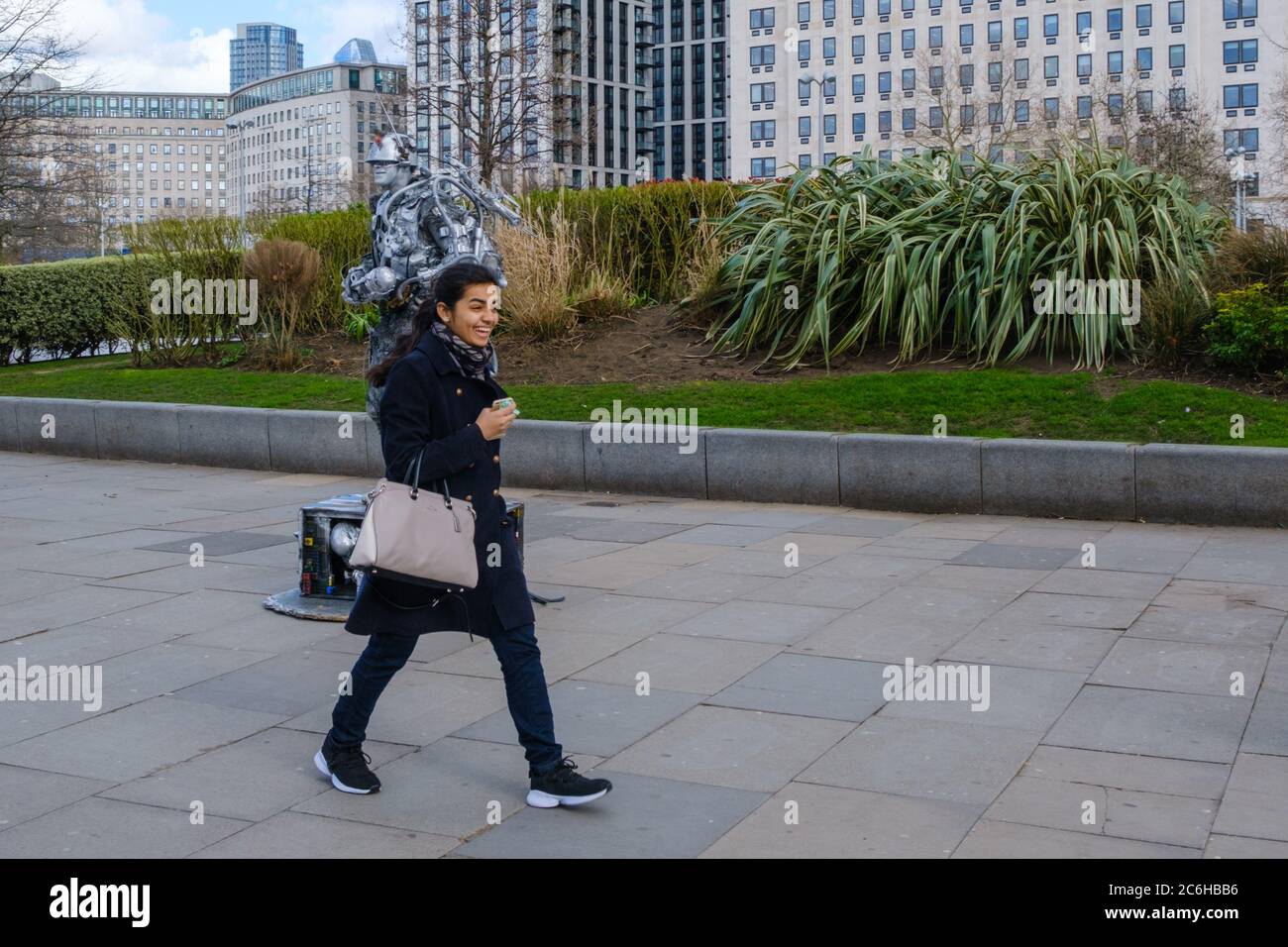 Süßer Moment, als junge lachende Dame an einer lächelnden Menschenstatue auf der Southbank in London vorbeigeht Stockfoto