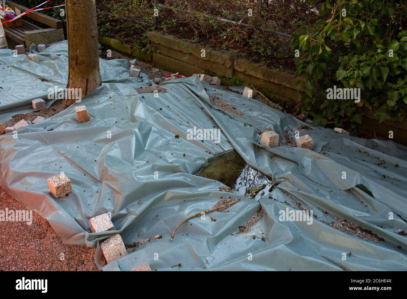 Kopfsteinpflaster wiegen ein Kunststoffblech ab, das eine Pflastersteinbaustelle bedeckt Stockfoto