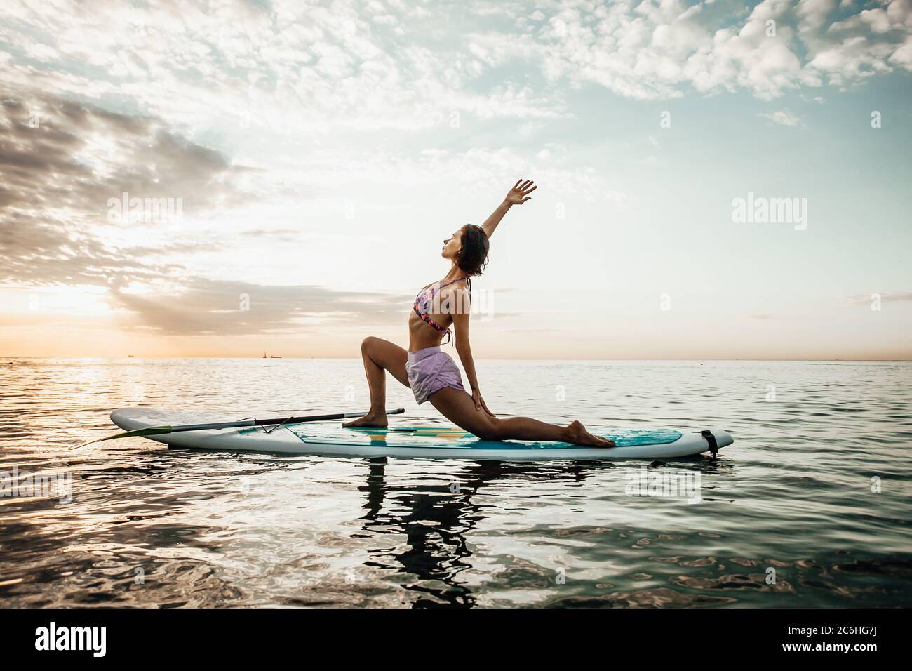 Junge Frau beim Yoga auf einem SUP-Board im See bei Sonnenaufgang Stockfoto