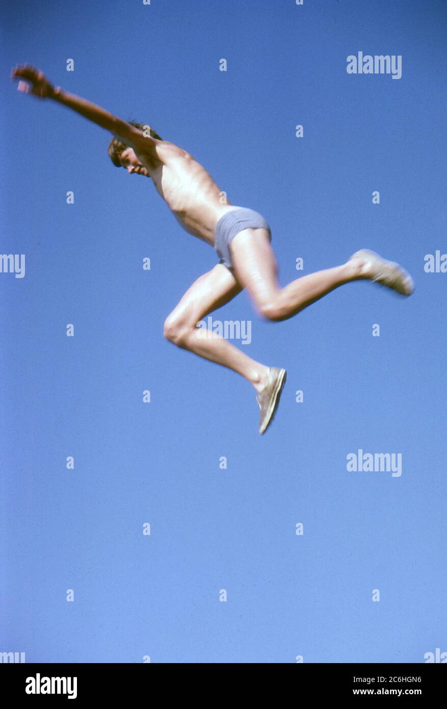 England. 1964. Ein Junge in Badehosen und Turnschuhen springt durch die Luft. Stockfoto